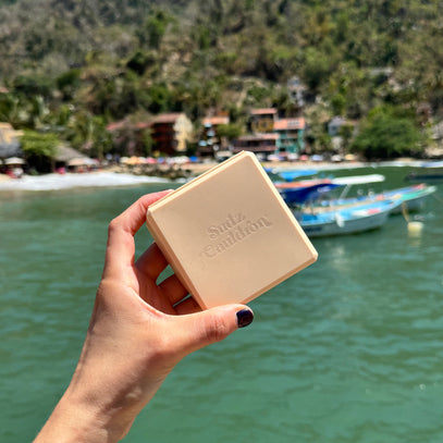 Hand holding a beige travel bar case with Sudz Cauldron brand logo against a scenic background of water and trees.